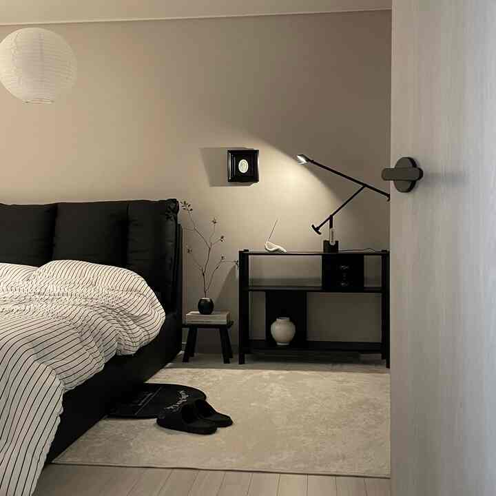 ブラックとホワイトのトーンの寝室、モダンなブラックのテーブルランプとベージュのラグが配置されたシンプルで落ち着いた雰囲気のあるインテリア