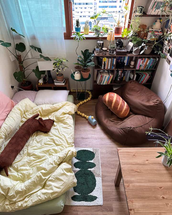 木目調の床とビーズクッション、ベッド、植物が配置された居心地の良い小さな一人暮らしの部屋