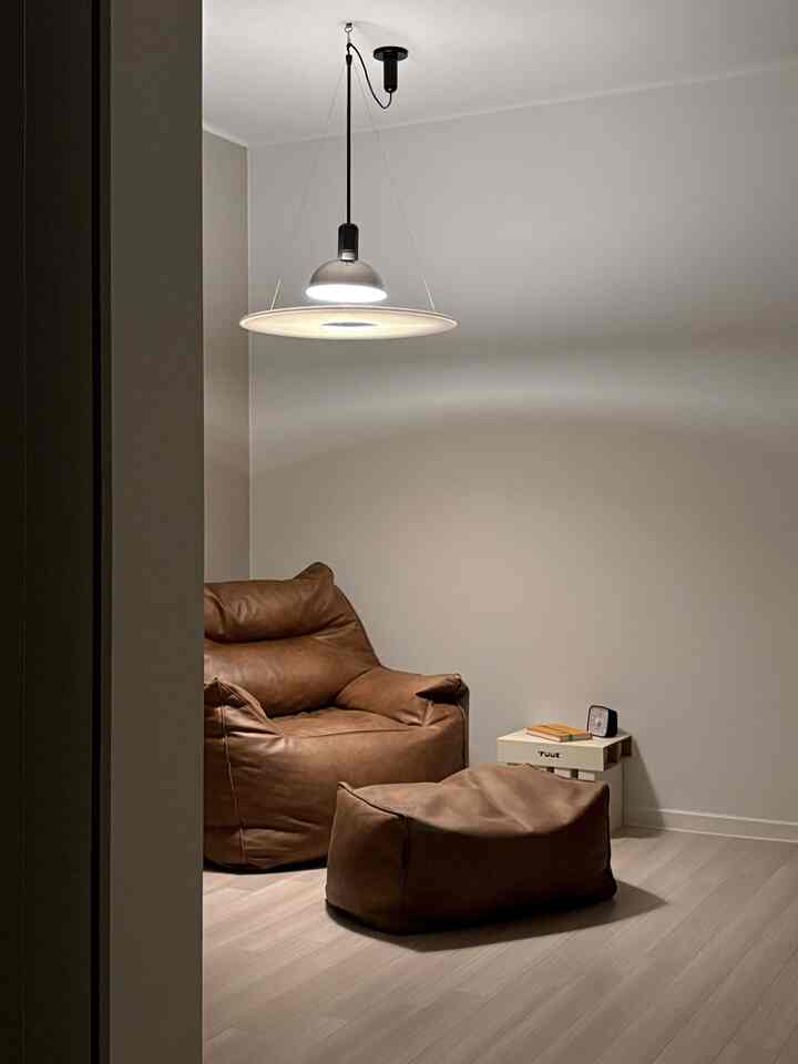 ナチュラルな色調のリビングの読書スペース、ブラウンレザーのビーンバッグソファとペンダントライトが配置された落ち着いた空間