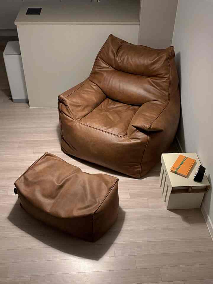Cozy white-tone small room featuring a brown leather bean bag sofa and matching stool