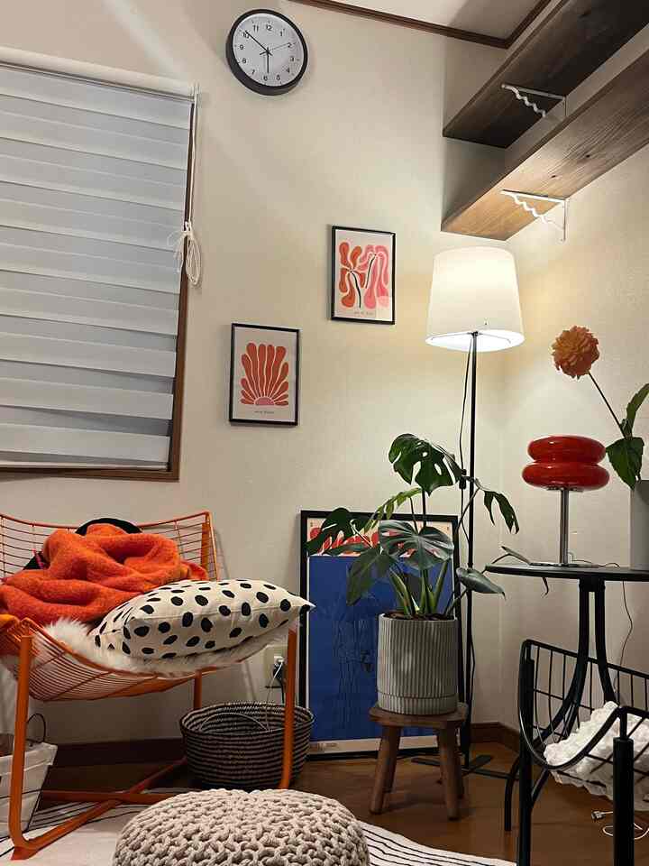 Cozy corner of a living room dominated by orange and white tones, featuring an armchair, floor lamp, plants, and framed artwork
