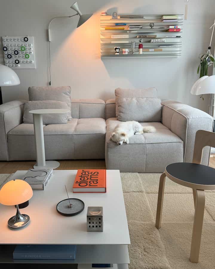 白とベージュの色調のリビング、モジュラーソファとラグ、壁棚と壁照明が配置された居心地の良いモダンなインテリア