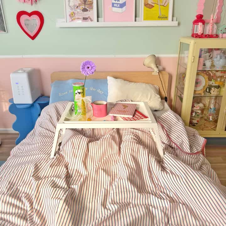 ピンクと白の色調の寝室、木製ベッドとストライプの掛け布団カバーが居心地の良い雰囲気を演出しているインテリア