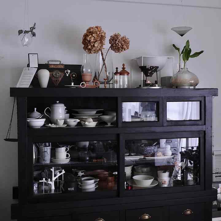 黒の食器棚が中心に配置されたナチュラルモダンな空間で、白い陶器とドライフラワーが飾られた落ち着いた雰囲気のインテリア