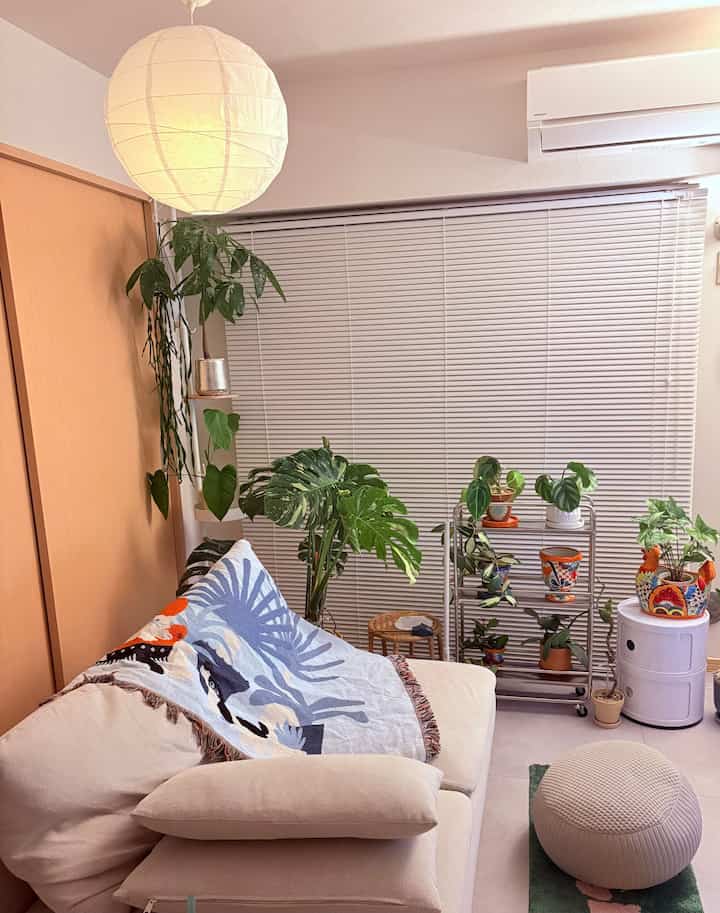 ナチュラルな色調の1LDKリビング、ベージュのソファと多くの観葉植物、紙製のペンダントライトが配置された雰囲気のある空間