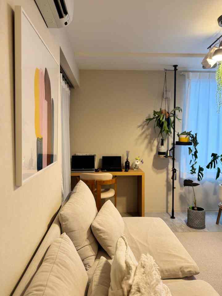 ベージュの色調が印象的な小さなリビング兼ホームオフィス、ソファと机、植物が配置された雰囲気のあるインテリア