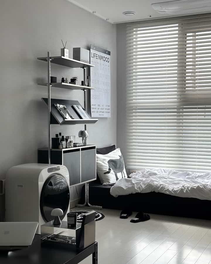 A modern small single household bedroom in white and black tones featuring blinds and minimal furniture