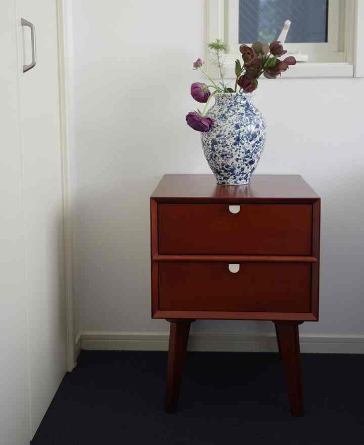 ネイビーのカーペットの上に茶色いサイドテーブルと青い模様の花瓶が置かれたシンプルな寝室のインテリア