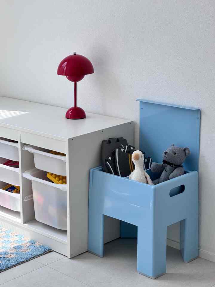 A white room with storage furniture and a vivid red lamp, featuring blue toy storage filled with stuffed animals