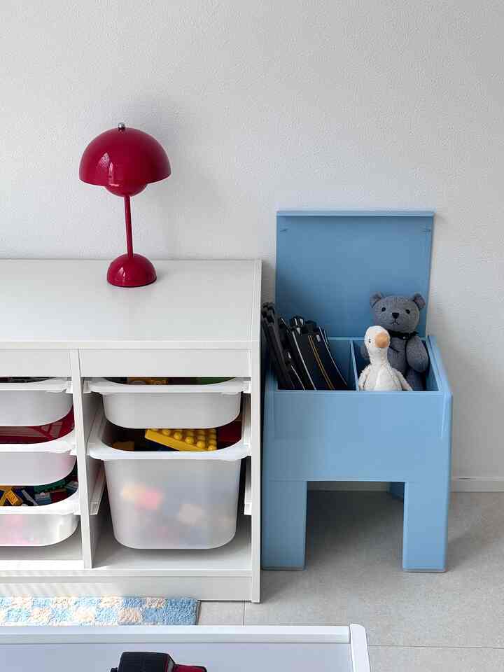 Bright white storage cabinet and pastel blue kids' storage stool with red table lamp in a tidy kids' room interior