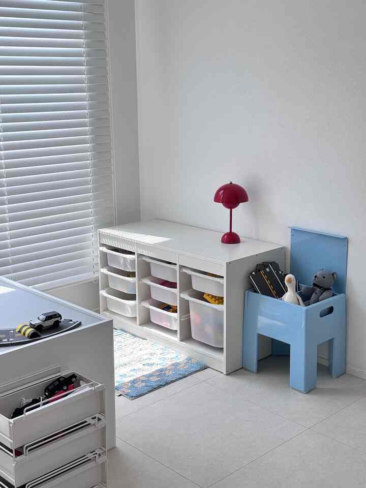 白い壁とブラインド、青い収納スツールと白い収納棚、子供のおもちゃが置かれた明るいプレイルーム