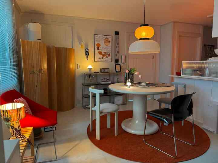 温かみのあるベージュと赤色調のダイニングルーム、白い円形テーブルと三種類の椅子が配置された居心地の良い空間