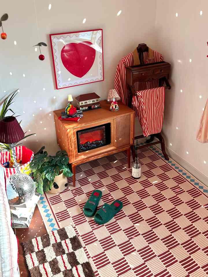 赤と木目調が調和したヴィンテージ風リビングの一角、ラグやテレビ台、ウォールアートが配置された温かみのあるインテリア