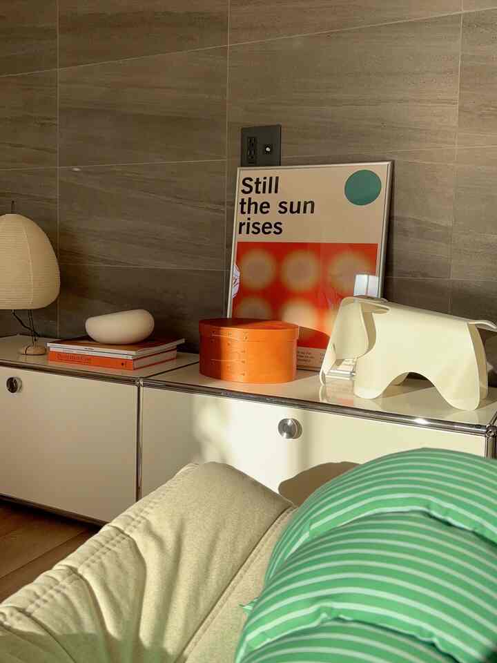 Warm beige and white toned living room featuring a USM TV board with a Vitra elephant stool and orange objet, simple modern interior