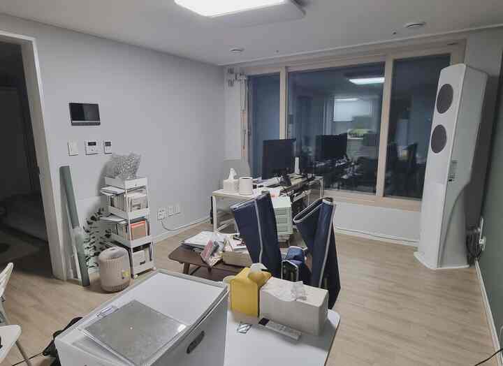 白と木目調が調和した狭い部屋のホームオフィス、デスクとデュアルモニター、移動式隙間棚が配置された整理中の雰囲気あるインテリア