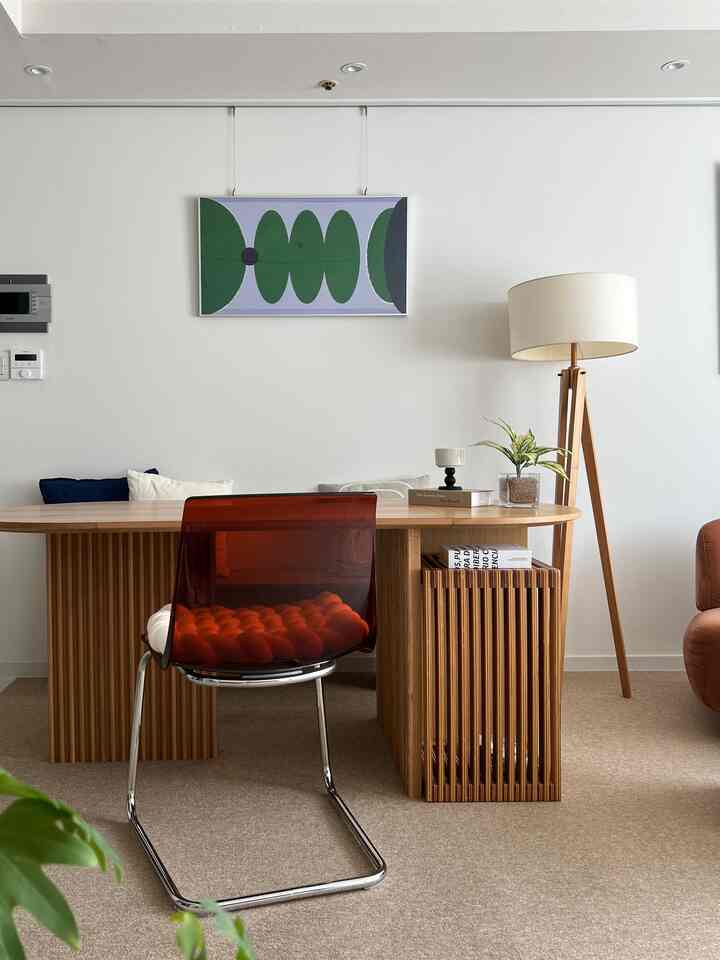 ベージュのカーペットと木目調家具が調和したシンプルなダイニング、透明な赤いダイニングチェアがアクセントの空間