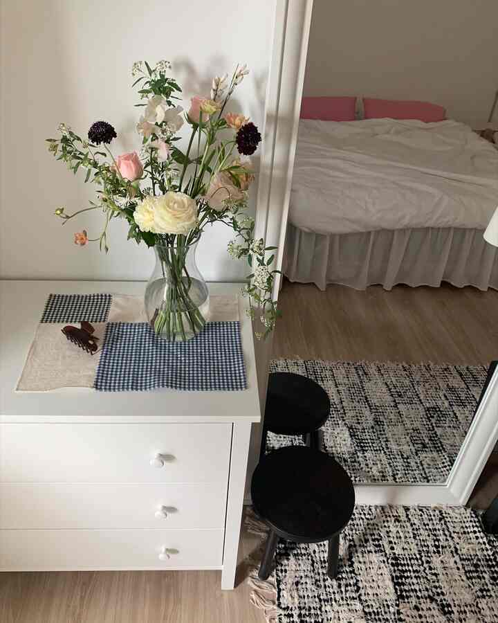 白と黒の色調の寝室、チェック柄のテーブルマットと花瓶が配置された自然な雰囲気のあるインテリア