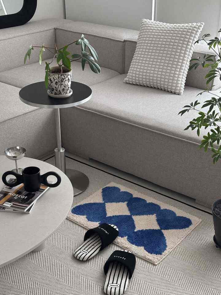 ライトグレーの色調のリビング、モジュラー型ファブリックソファと青のパターンのロングパイルラグが配置された自然で落ち着いた雰囲気のインテリア