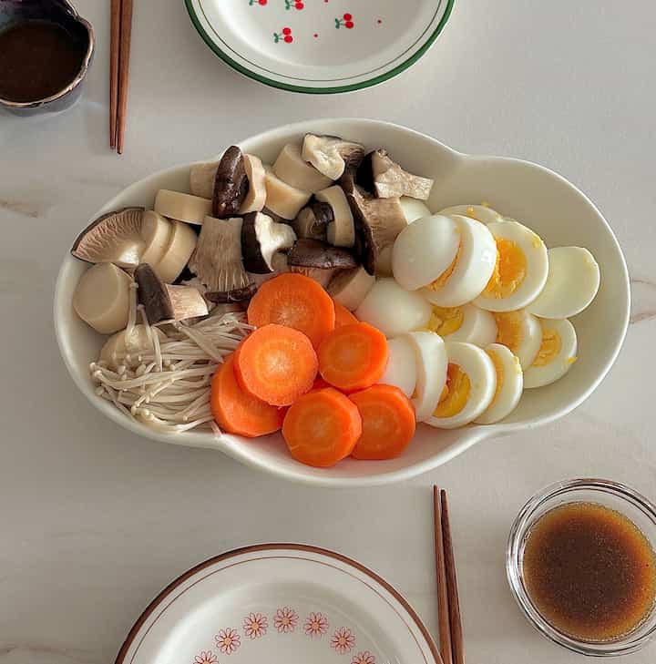 ナチュラルな色調のキッチンの食卓に、さまざまな野菜の蒸し物とゆで卵が盛られた白い皿が置かれた清潔感のある家庭料理の空間
