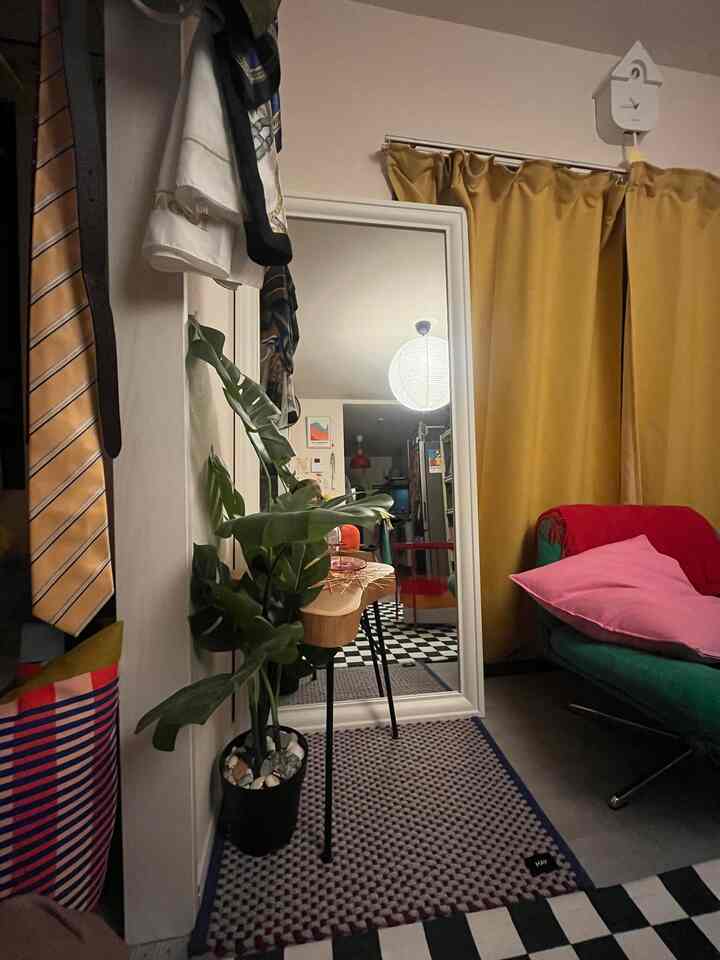 ゴールドのカーテンとグリーンのアームチェアがあるミッドセンチュリーモダンのリビング、大きな鏡と植物が配置された雰囲気のある空間