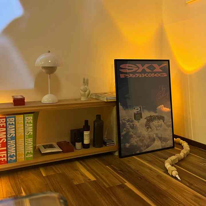 Warm yellow-lit space featuring wood tone shelves and table lamp with a natural art poster ambiance