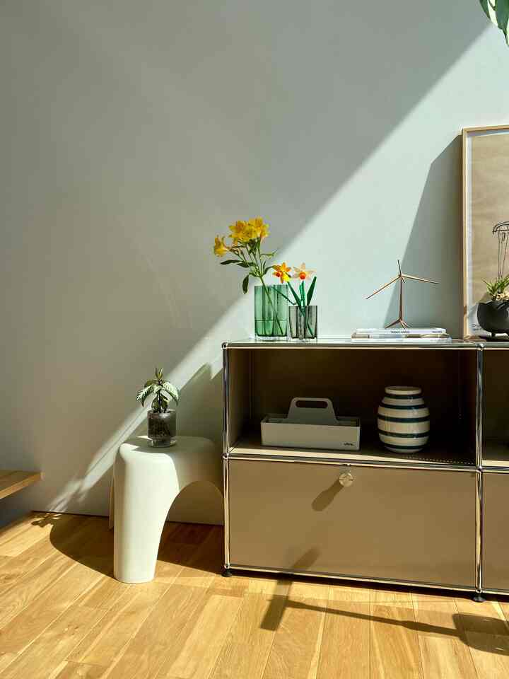 ナチュラルカラーと白が調和するリビング、ベージュのサイドボードと白いスツール、植物が配置された落ち着いた雰囲気のインテリア