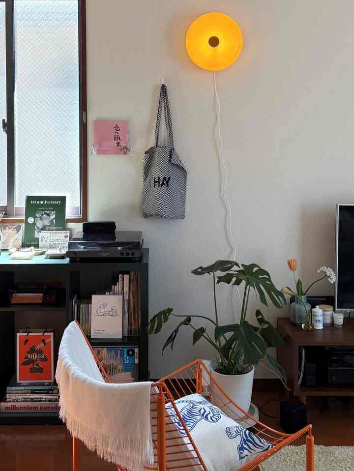 明るくナチュラルな色調の1LDKリビング、オレンジのアームチェアとモンステラの植物が配置された印象的な空間