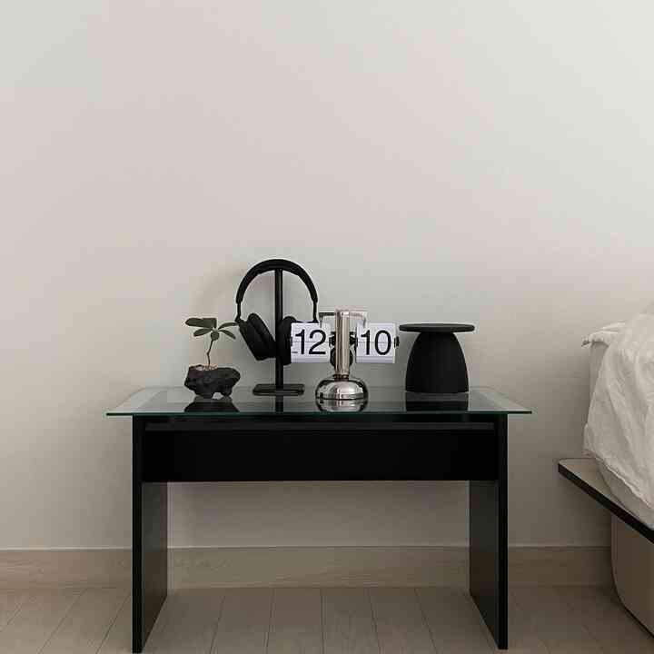 白い壁を背景に黒いナイトテーブルとヘッドフォン、時計が置かれた寝室空間