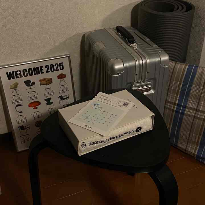 Charcoal and black toned small entrance space featuring mid-century modern stool, silver suitcase, and calendar in cozy corner