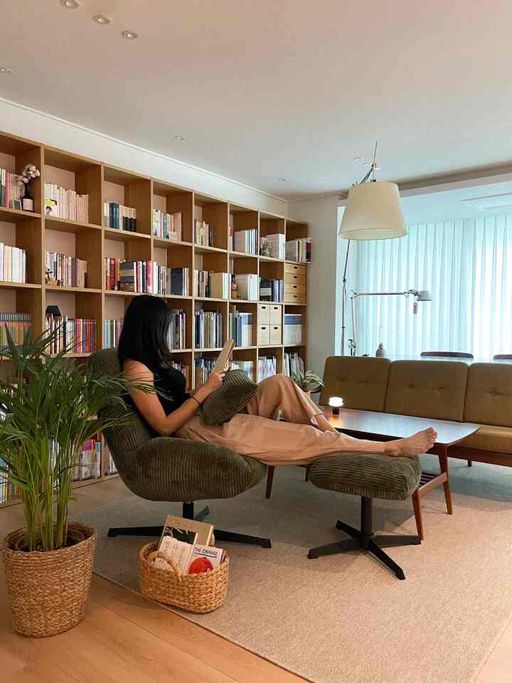 穏やかなナチュラルカラーのリビング書斎、オリーブグリーンのアームチェアと大型本棚が配置された落ち着いた読書空間