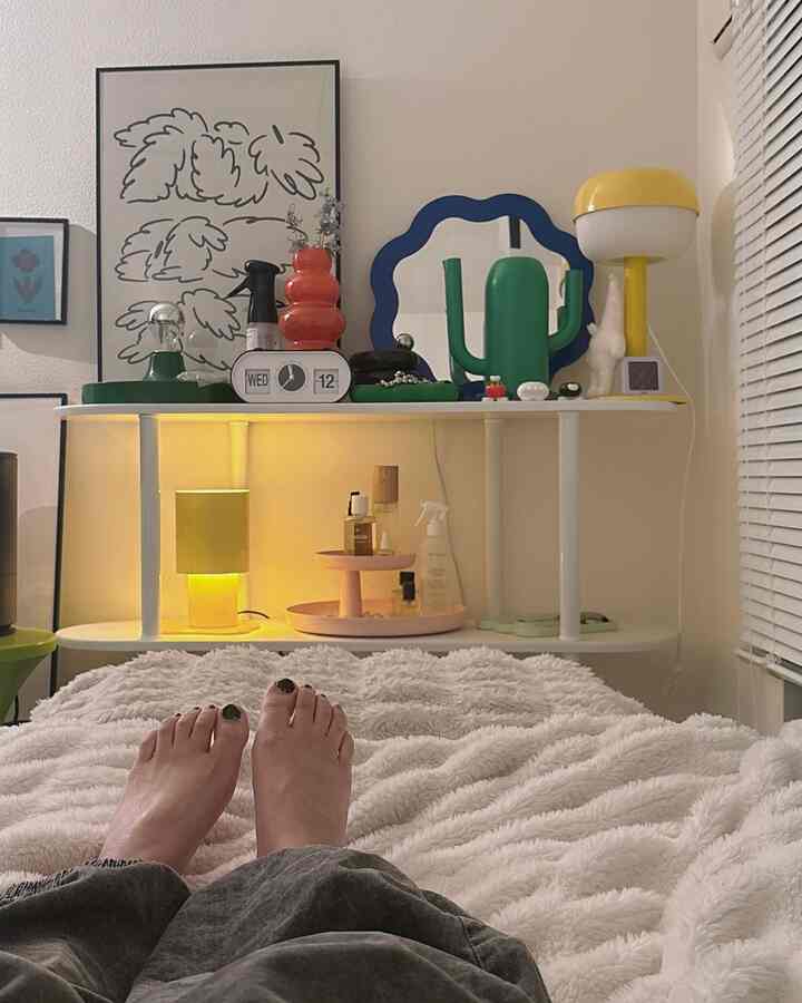 White-toned 8-tatami bedroom featuring a bed, shelf with posters and a yellow table lamp, creating a cozy Korean interior vibe
