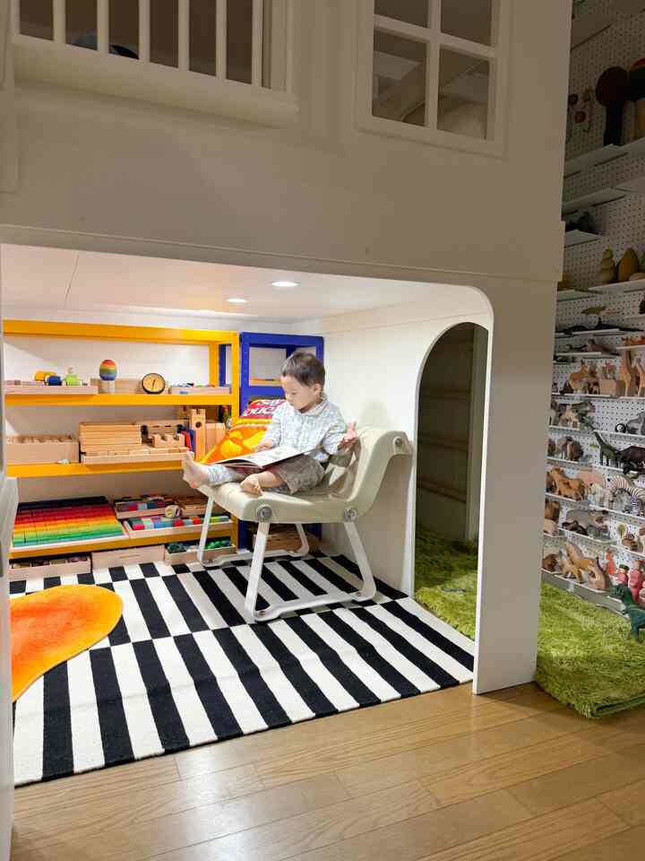 白と木目調の調和がとれた子供部屋、白黒のストライプラグとカラフルな棚に本とおもちゃが整頓された雰囲気のある空間