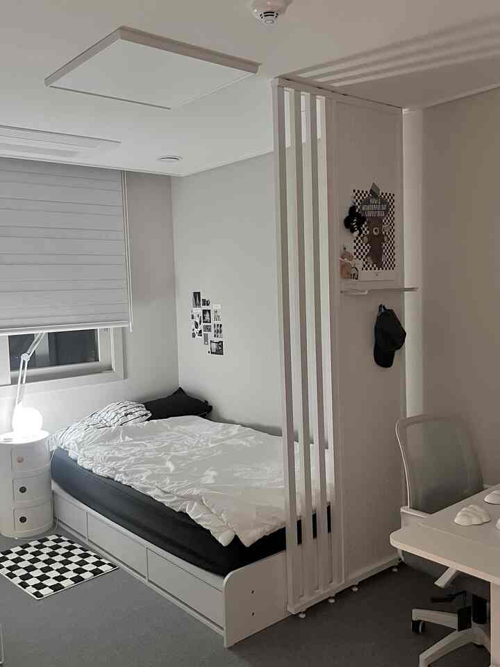 ホワイトとグレーの色調の小さなワンルーム寝室、ベッドとデスク、仕切りパネルが配置されたモダンなホームオフィス空間