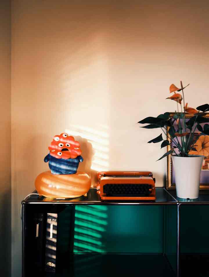 暖かいオレンジと木目調が調和したミッドセンチュリーモダンの空間、ビンテージタイプライターと可愛らしいインテリア小物が配置された雰囲気のあるインテリア