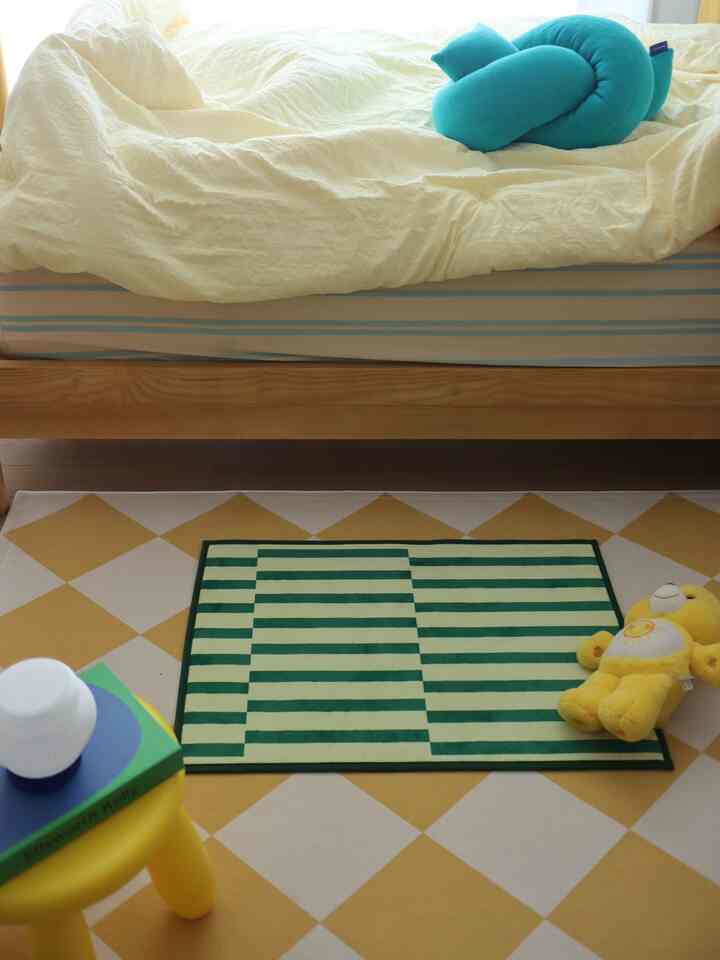 白と黄色のトーンの子供部屋、ベッドの下にさまざまなパターンのラグと黄色のぬいぐるみ、黄色のスツールが配置された温かみのある空間