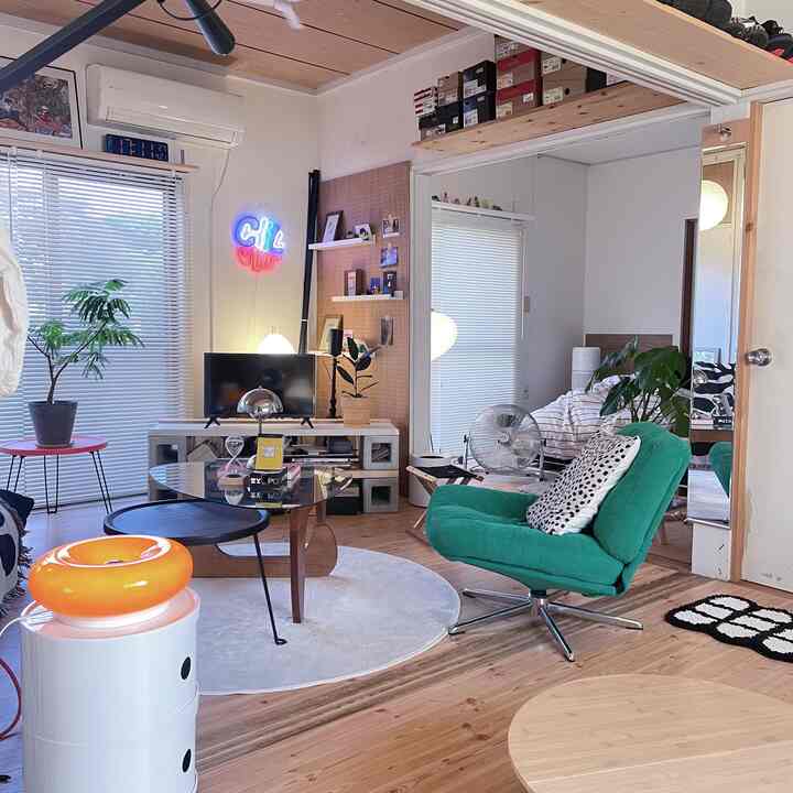 ナチュラルウッド調のリビング、グリーンのアームチェアとガラスのコーヒーテーブルが配置されたミニマルで清潔感のあるインテリア