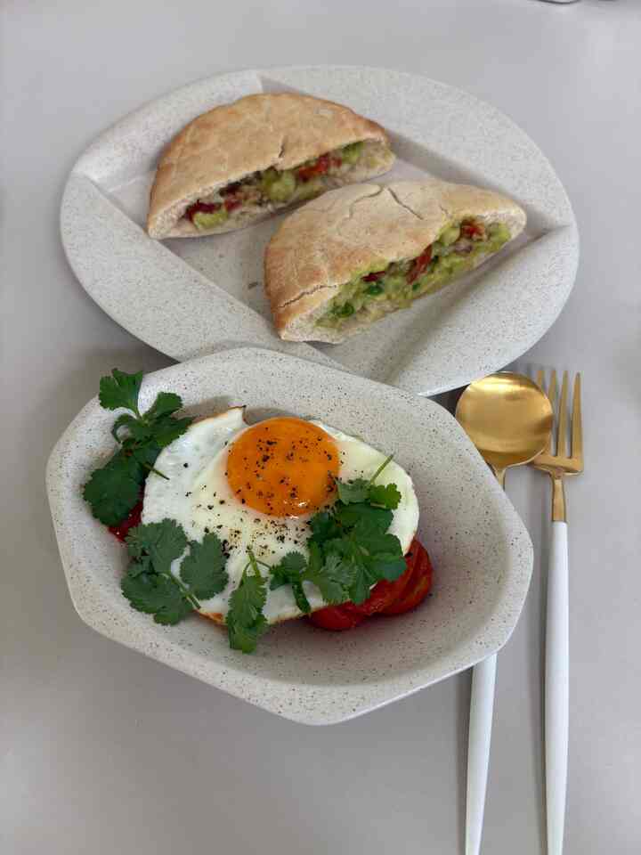 白い背景にナチュラルトーンの皿、トマトと半熟卵、グアカモレが並ぶシンプルな朝食