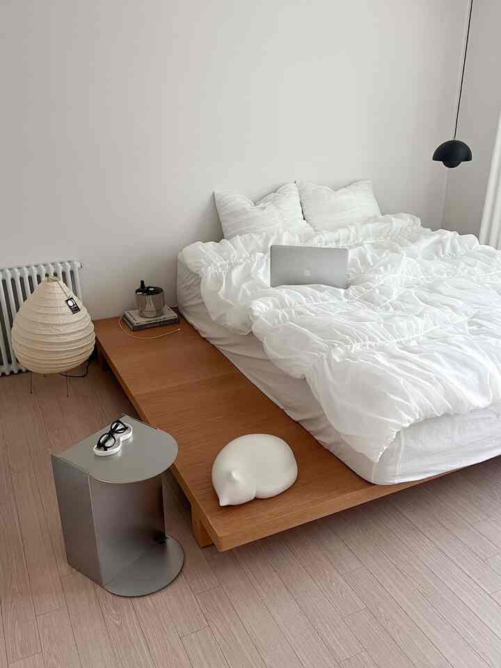 Modern bedroom with harmonious white and wood tones, featuring a platform bed, side table, and floor lamp in a clean space