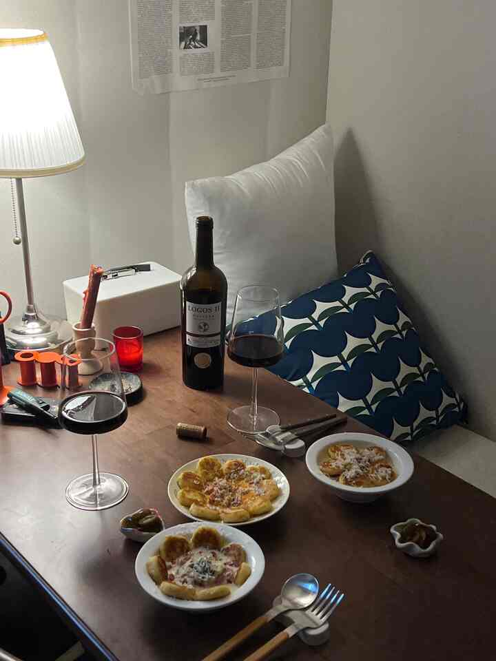 暖かみのあるブラウンの木製ダイニングテーブルと白い壁、ワイングラスと皿があるワンルームのダイニングスペース