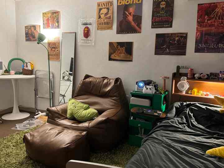 緑と茶色のトーンが特徴のワンルーム、ビーズクッションのソファとベッドが配置され、壁にはポスターが飾られた雰囲気のあるインテリア