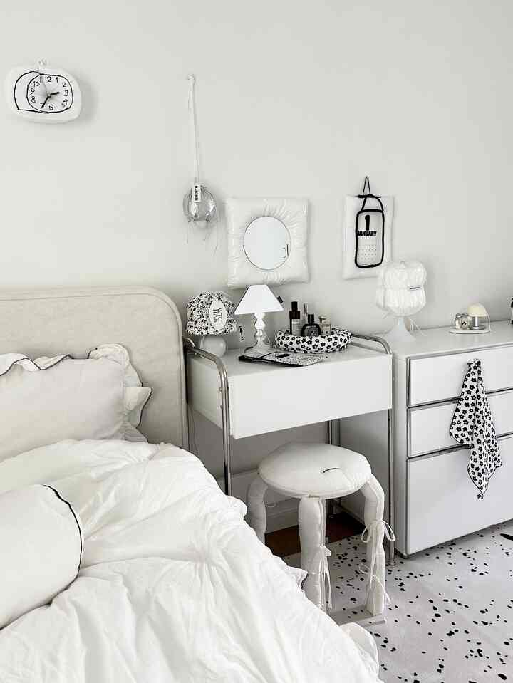 白を基調とした寝室、白いベッドとナイトテーブル、小さなテーブルランプとパターンカーペットが配置されたシンプルな空間