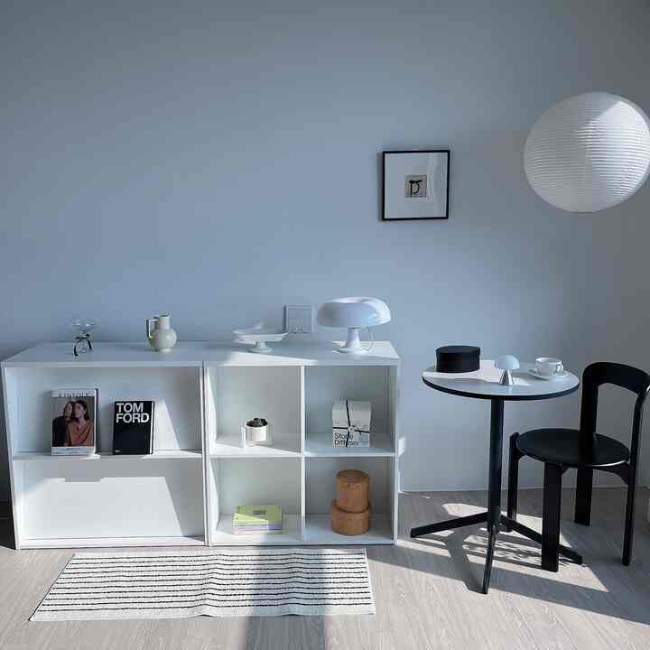 A compact living room in white and black tones featuring a modern dining table, chair, and decorative objects in a tidy setting