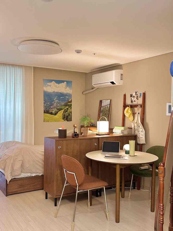 ライトブラウンの壁と木目調家具が配置されたワンルーム、木製テーブルと椅子、温かみのあるスタンドランプが調和する雰囲気のあるインテリア