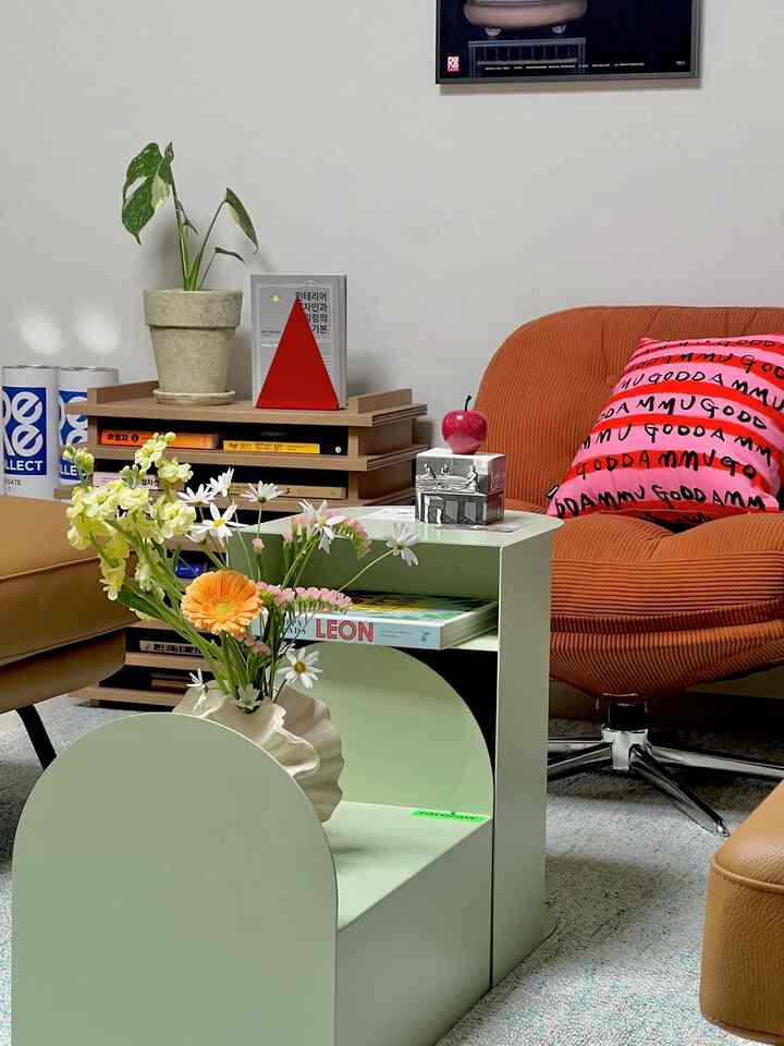 ベージュの壁とナチュラルトーンの家具が配されたリビング、目立つオレンジのアームチェアと淡い緑のコーヒーテーブルが温かみのある雰囲気を演出