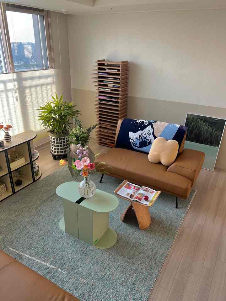 ナチュラルな木目調とブラウンのソファが配置された明るいリビング、ミントグリーンのプリットテーブルと植物が印象的な居心地の良い空間