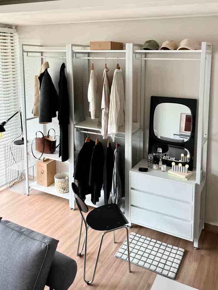 白とナチュラルトーンのウォークインクローゼット、清潔感のあるシステムハンガー、ドレッサー、黒い椅子、鏡が配置されたモダンなインテリア