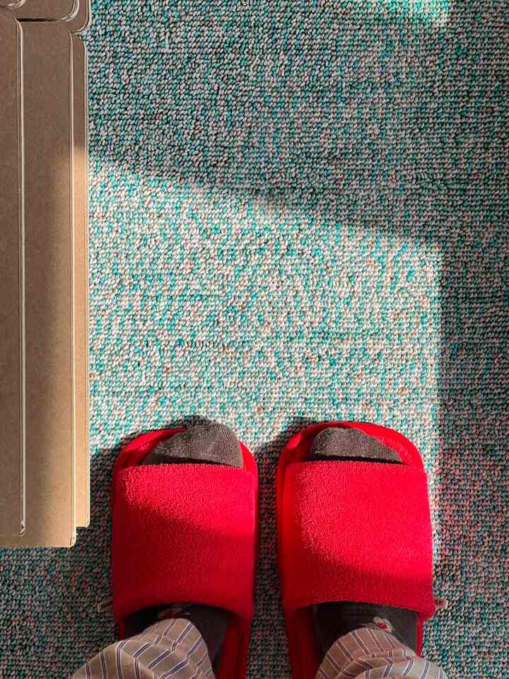 明るい赤のスリッパがパステルトーンのラグの上にある、温かみのあるホームオフィスの空間