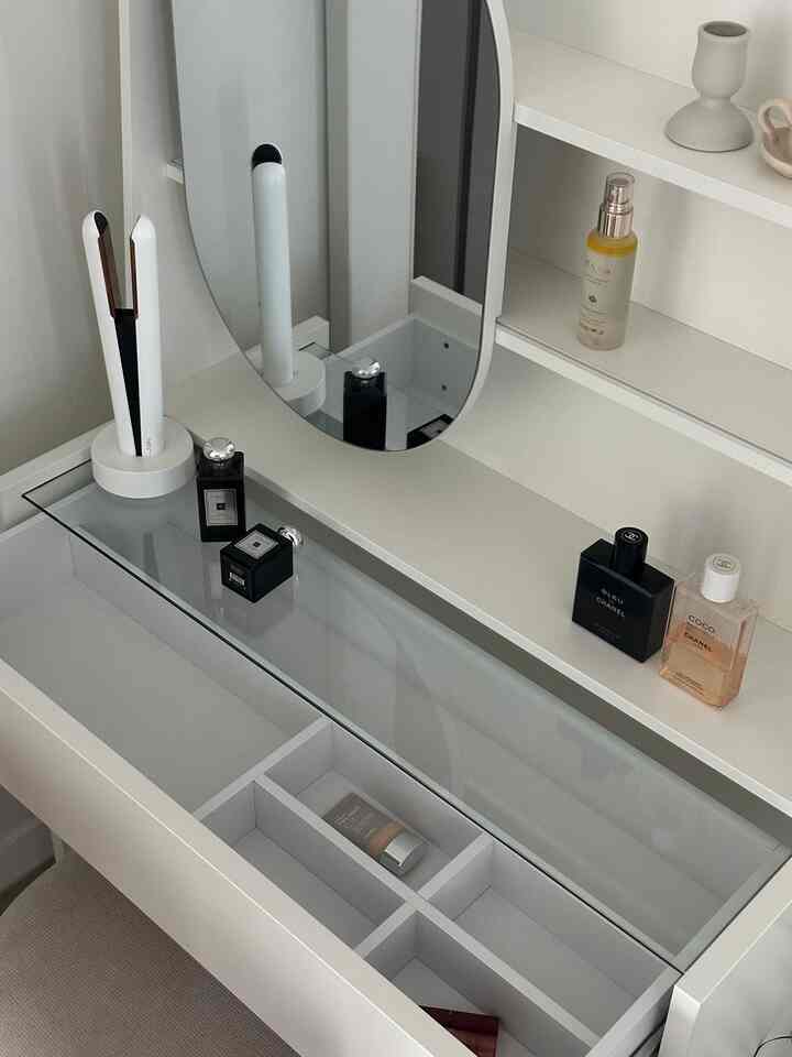 透明なガラストップとホワイトトーンのミニマルモダンな化粧台が、美しく整頓されたビューティーアイテムとともに配置された寝室家具