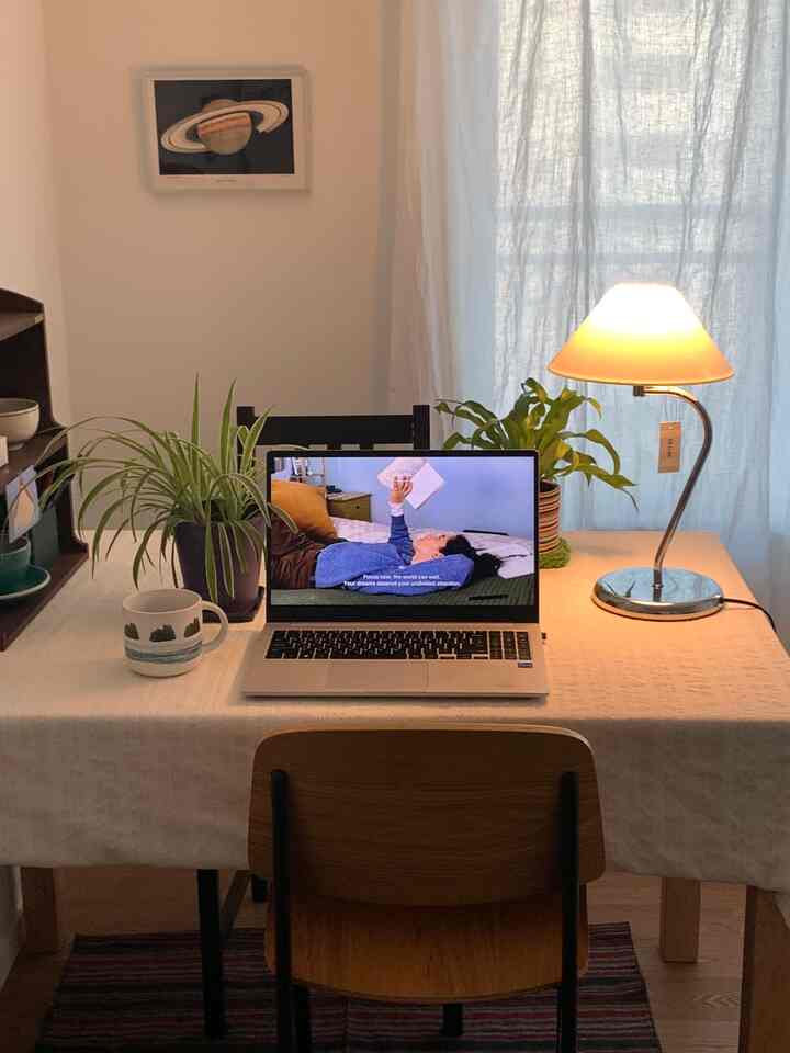 アイボリー色のテーブルクロスの上にシルバーボディとアイボリーシェードのテーブルランプが置かれた、ノートパソコンのある雰囲気のある寝室のデスク