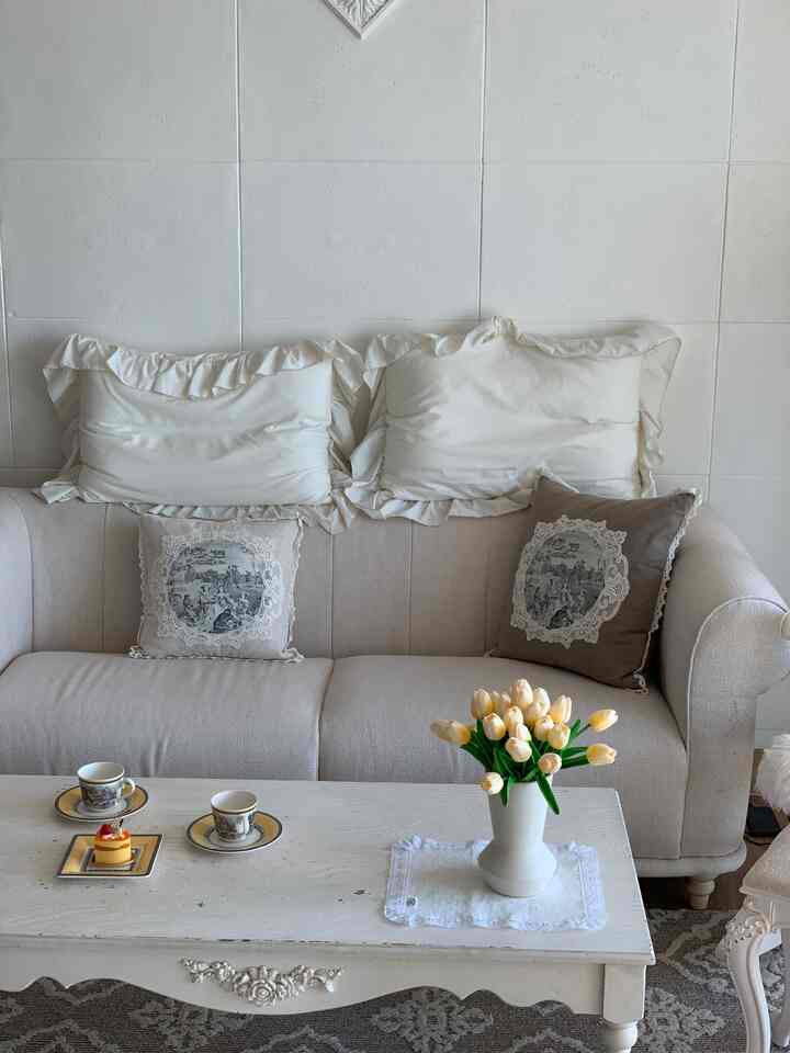 White and beige toned living room featuring an antique style sofa and coffee table, cozy atmosphere with vase and cushions